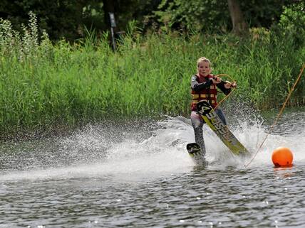 Am Rumpelsee bei Süsel (Ostholstein) steht Keana Straatmann (18) aus Kiel auf dem Steg und zieht die Wasserski an. Füße samt Ski ins Wasser, an der Leine festhalten – und los. Schnell ist der See umrundet und Keana kommt glücklich ans Ufer. „Das macht einfach mega Spaß“, findet sie. „Die Geschwindigkeit und mit dem ganzen Körper zu hüpfen, in die Kurven zu gehen ist ein tolles Gefühl.“ Auch ein bisschen anstrengend: „Der ganze Körper wird gefordert, jeder Muskel angespannt.“Da Keanas Großmutter in der Nähe lebt, ist die Schülerin aus Kiel öfter in Süsel und am Rumpelsee. Dort vermietet Christian Rumpel (41) Wasserski. „Mein Großvater hat den See ausgebaggert“, erzählt er. „Ursprünglich zur Kiesgewinnung.“ Seit 34 Jahren ist dort nun ein beliebtes Wassersportparadies mit drei Ski-Anlagen. Am Wochenende kommen täglich bis zu 300 Leute. „Am Sonntag öffnen wir um 12 Uhr“, sagt Christian Rumpel. Eine Zwei-Stunden-Karte kostet 35 Euro.